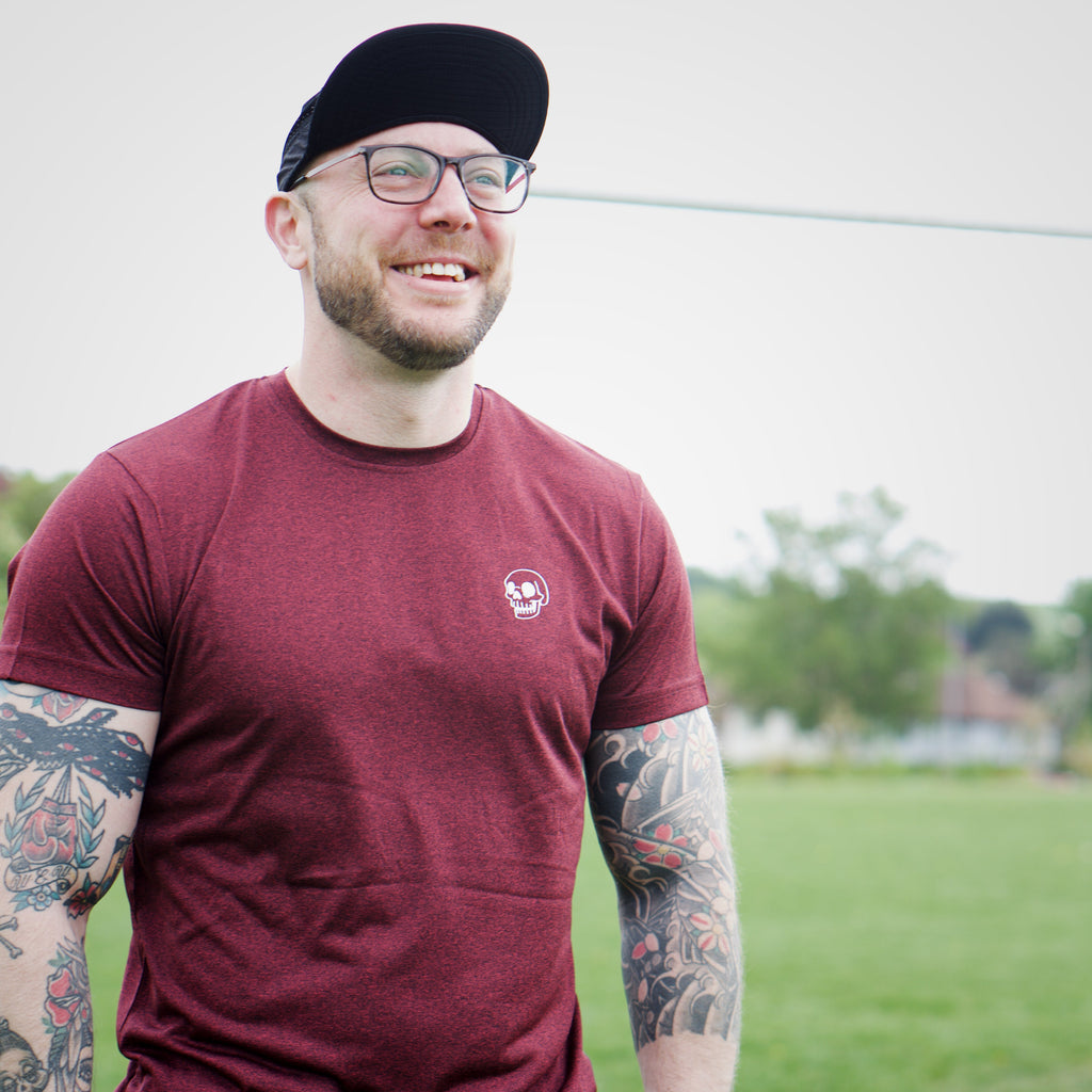 Man wearing a maroon t-shirt and black cap standing on a grassy field.